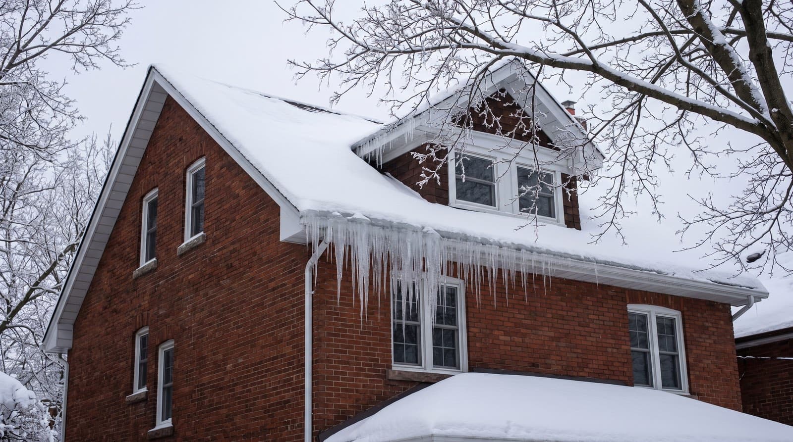 A snow-laden roof on a Toronto house with large icicles and an ice dam forming along the eaves in winter